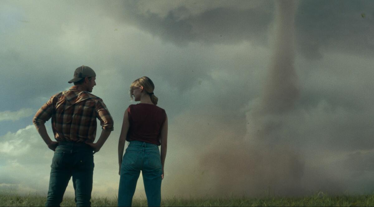 A man and a woman stand discussing the giant tornado in front of them.