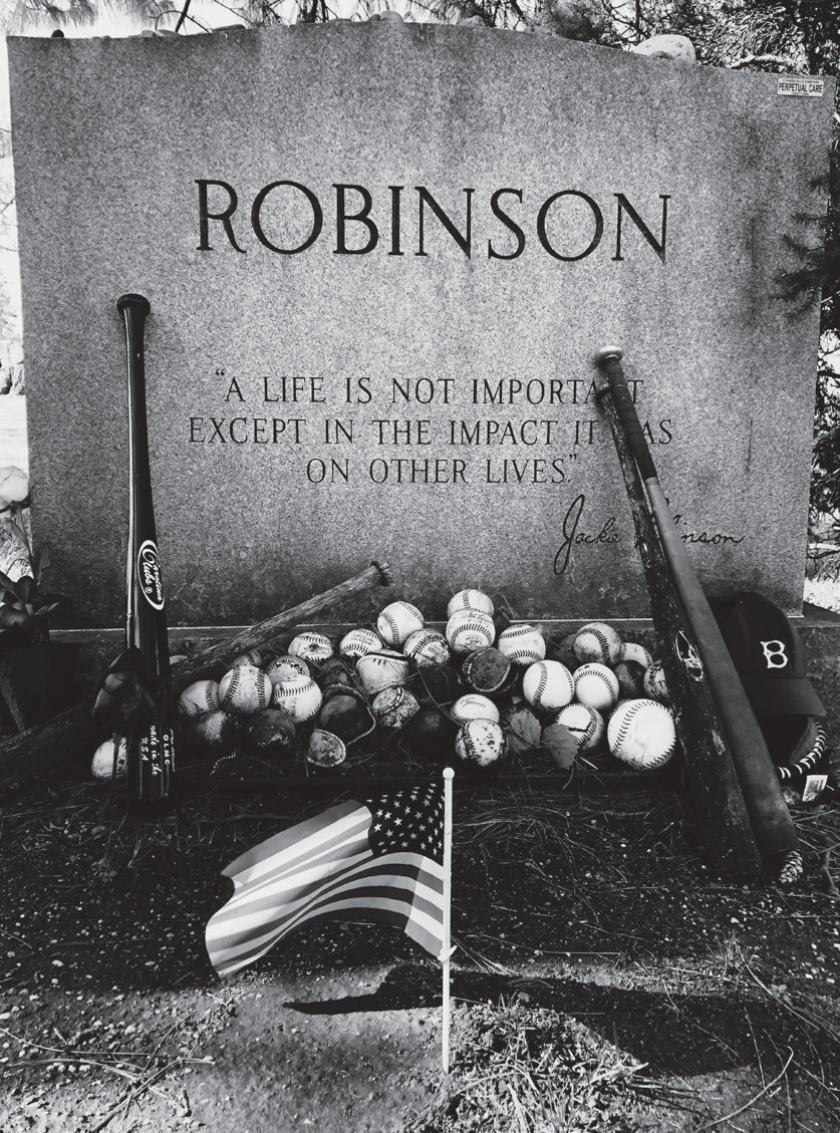 Robinson's gravestone with baseballs, bats and a small American flag in front of it.