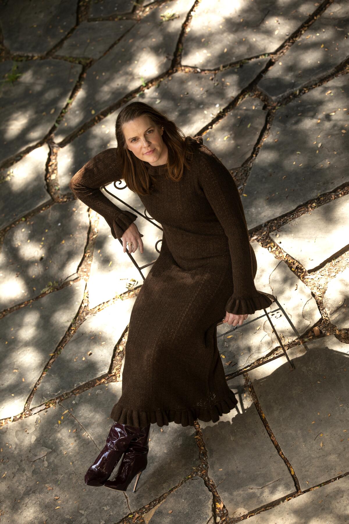 Film editor Jennifer Lame wears a long dress and sits on a broken-concrete patio for a portrait.
