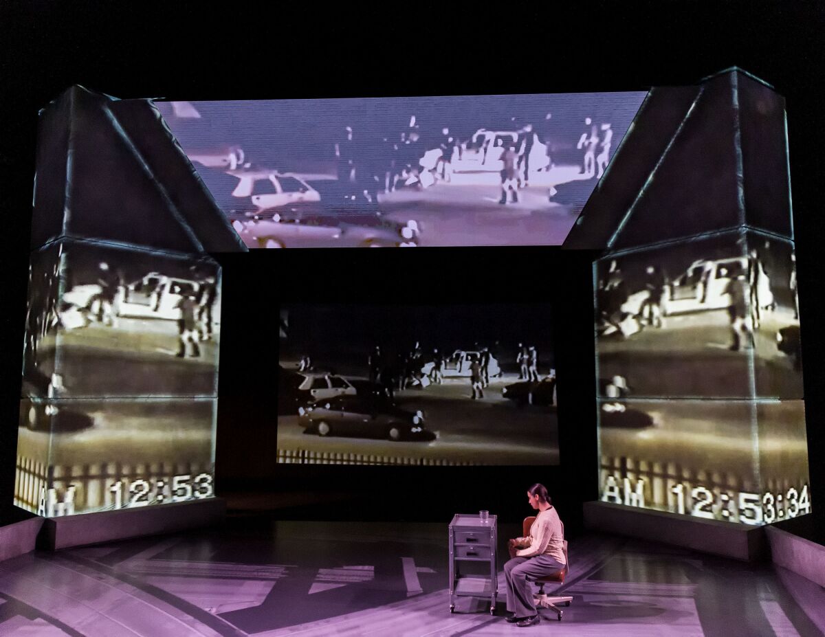 A person seated on a stage surrounded by digital projections of street scenes