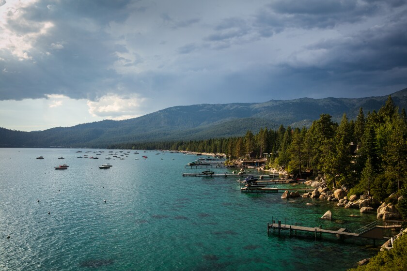 Lake Tahoe shore with underwater boats, trees and large rocks along the shore.