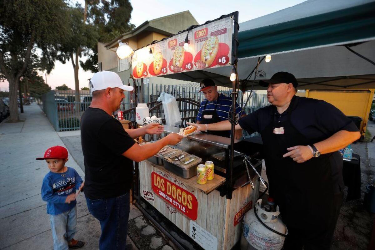 Alejandro Zamorano, right, and his nephew David Zamorano serve Sonoran-style hot dogs at their cart in front of a friend's house in Compton.