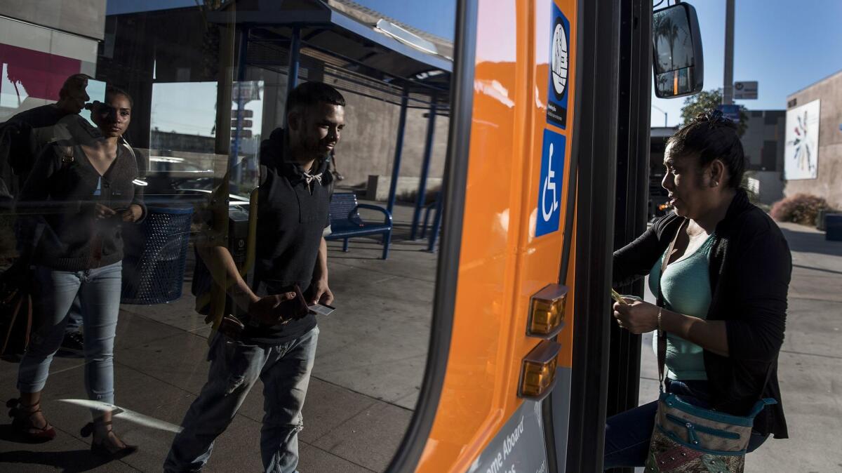 Bus riders Josh Ayala, 18, center, and Hazel Hernandez, left, are reflected in the window of a bus at Firestone and Atlantic boulevards in South Gate.