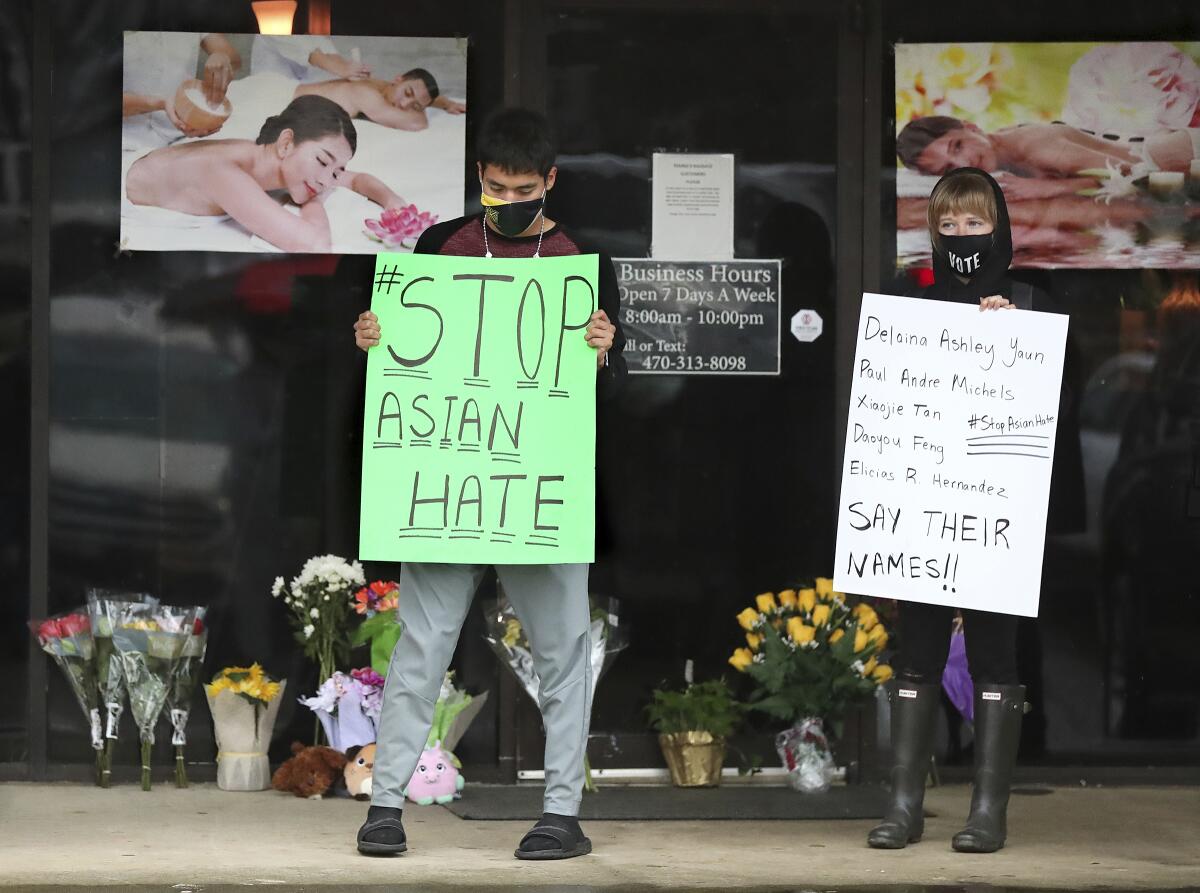 Two people stand outside a building with flowers, with one person holding a sign that says "stop Asian hate."