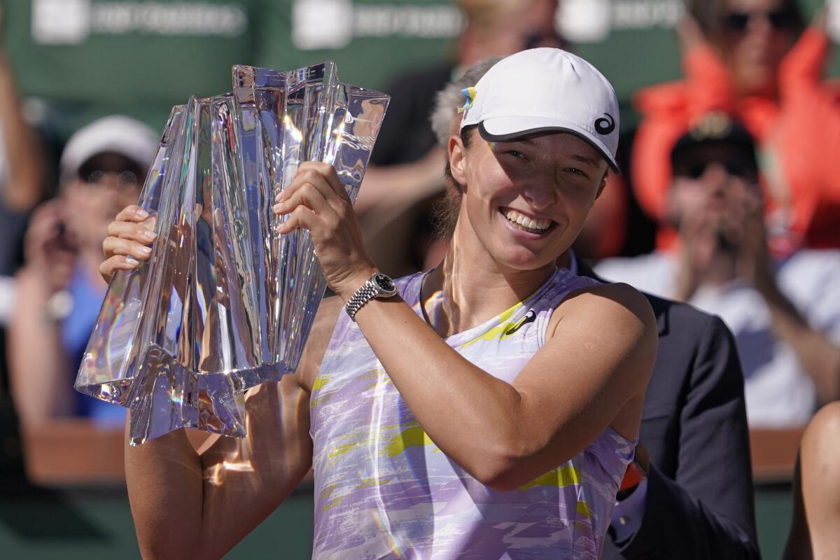Iga Swiatek smiles as she holds her trophy after defeating Maria Sakkari.