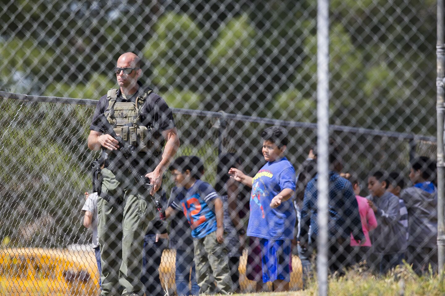 A SWAT officer stands guard with evacuated children on the playground at North Park Elementary School in San Bernardino after a shooting in the school.