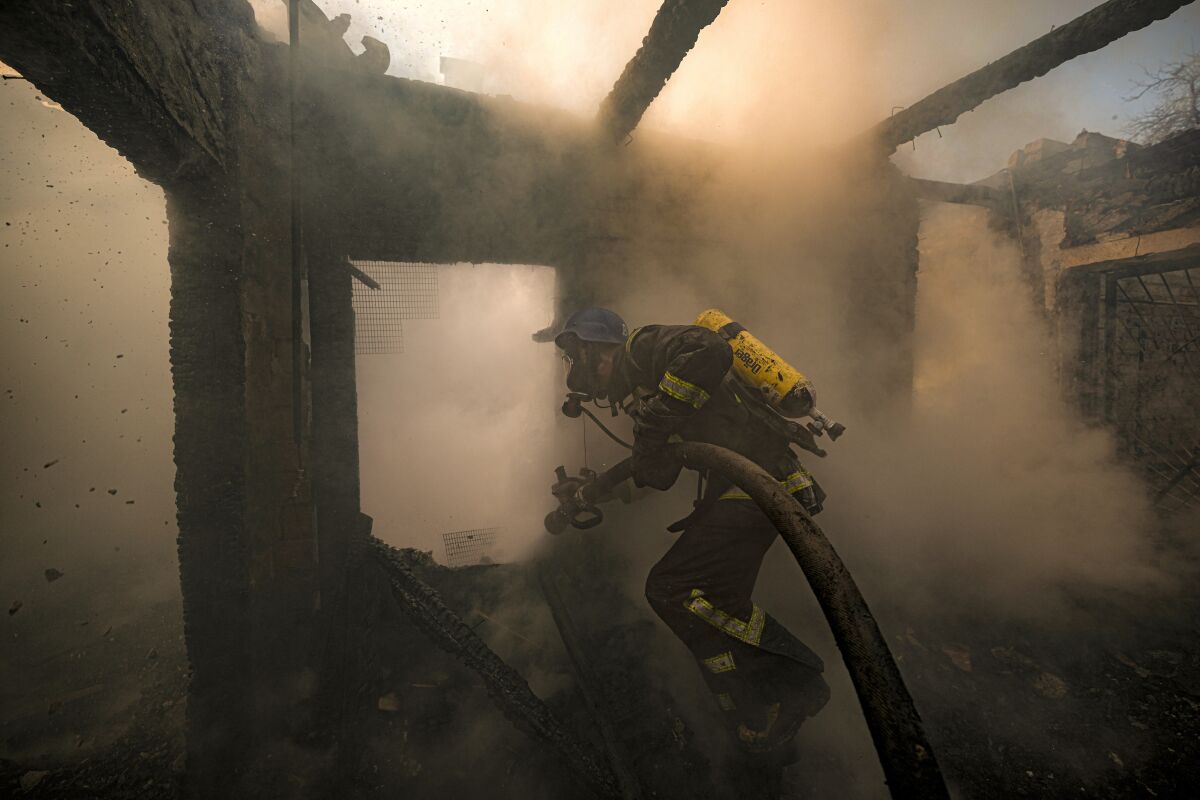 A firefighter sprays water from a black hose as smoke swirls around him in a destroyed structure