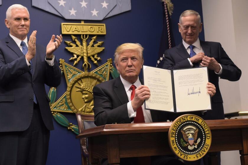 President Trump, flanked by Vice President Mike Pence, left, and Secretary of Defense James Mattis, shows his signature on executive orders signed Jan. 27. One of the orders banned people from seven predominantly Muslim nations from traveling to the United States.