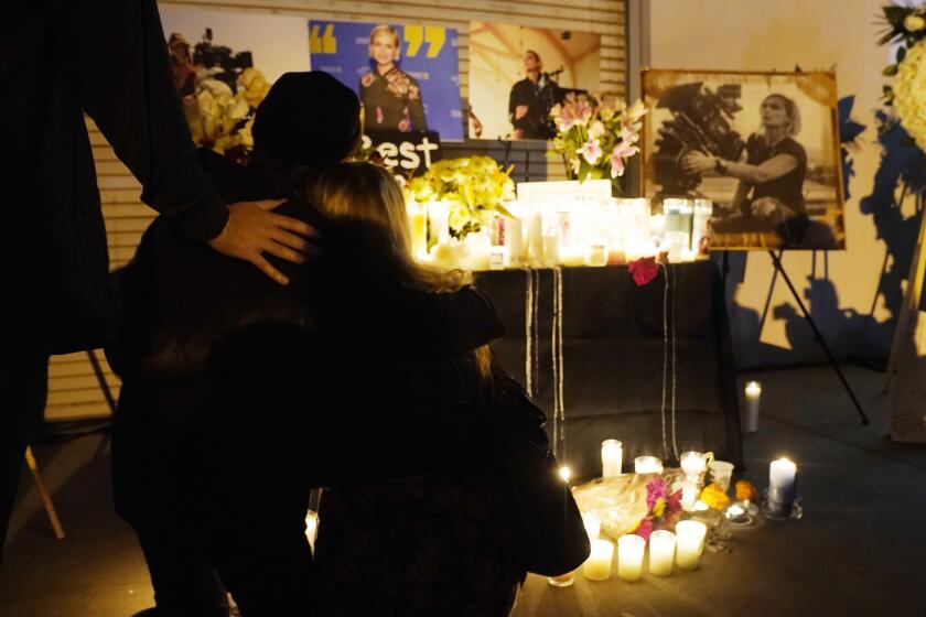 Asistentes se abrazan en una vigilia por la fallecida directora de fotografía Halyna Hutchins, representada en fotografías al fondo, el domingo 24 de octubre de 2021, en Burbank, California. Un arma de utilería disparada el jueves por el actor Alec Baldwin en el set de una película en Santa Fe, Nuevo México, mató a Hutchins e hirió al director Joel Souza. (Foto AP/Chris Pizzello)