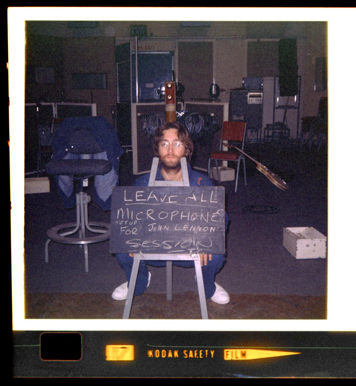 John Lennon poses with a chalkboard reminding EMI Studios staff to "Leave all microphones set up for John Lennon session."