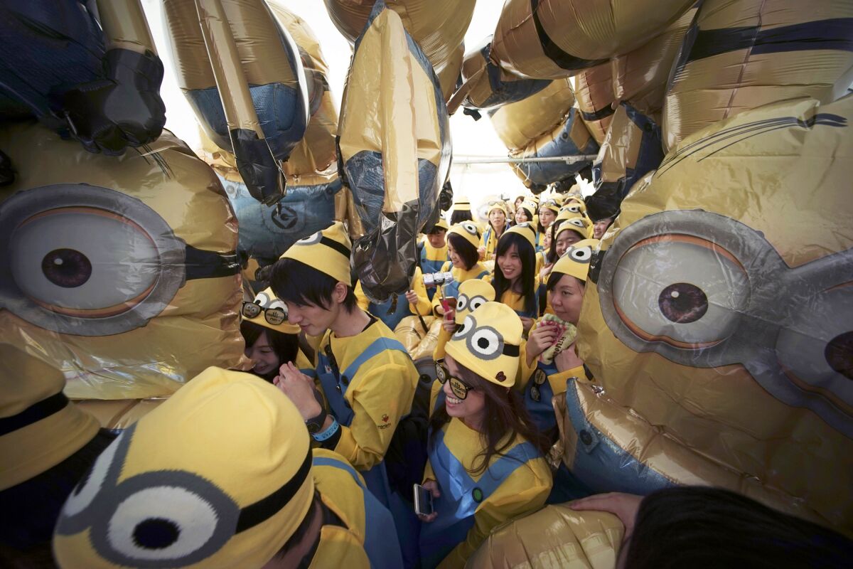 FILE - Participants dressed as minion characters from the "Despicable Me" franchise walk through minion balloons during the Minions Run in Tokyo on Feb. 13, 2016. This summer, the goggle-wearing yellow ones will return in “Minions: Rise of Gru," in theaters July 1. The “Despicable Me” franchise and its “Minions” spinoffs are the highest grossing animated film franchise ever with more than $3.7 billion in tickets sold worldwide. (AP Photo/Eugene Hoshiko, File)