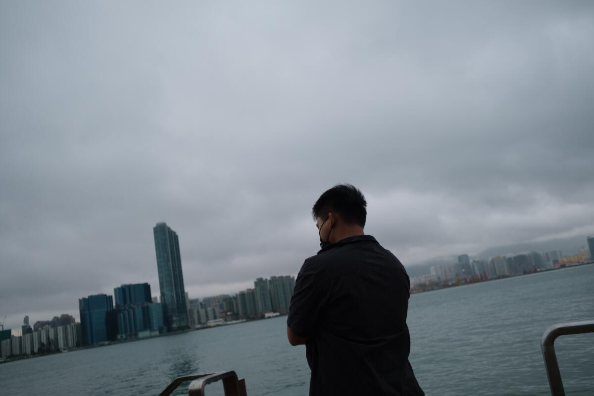 A man faces the water, with a city skyline in the distance