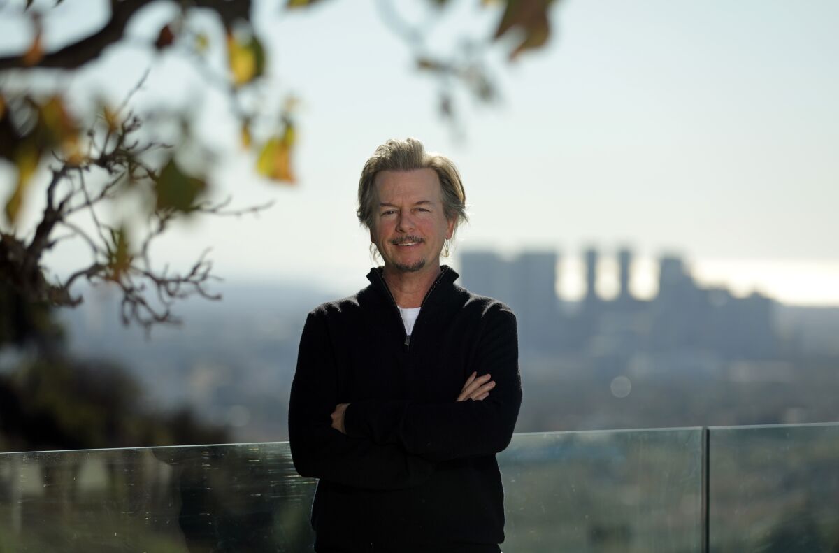 David Spade outdoors, with a skyline out of focus behind him in the distance.