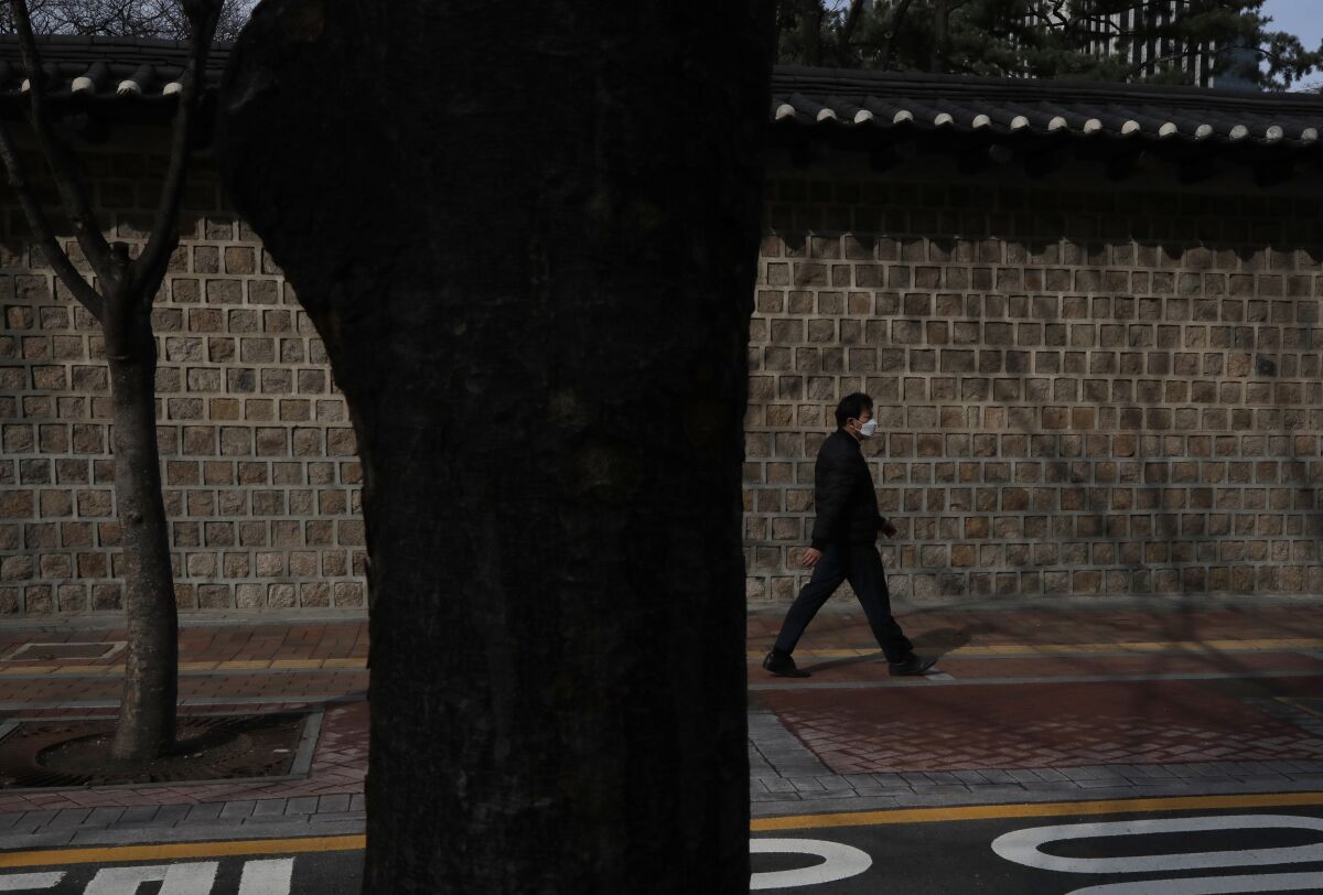 A man wearing a face mask walks along a wall outside the Deoksu palace in downtown Seoul, South Korea, Friday, March 13, 2020. For most people, the new coronavirus causes only mild or moderate symptoms, such as fever and cough. For some, especially older adults and people with existing health problems, it can cause more severe illness, including pneumonia. (AP Photo/Lee Jin-man)