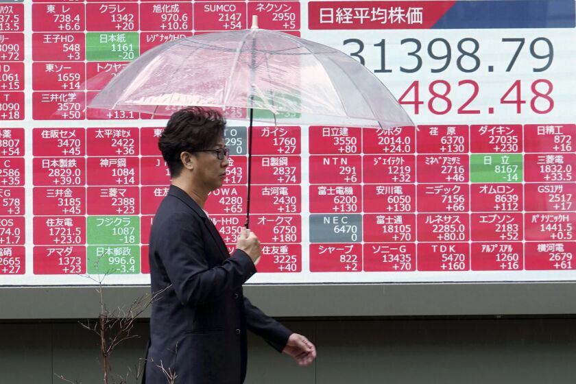 A person walks in front of an electronic stock board showing Japan's Nikkei 225 index at a securities firm in the rain Monday, May 29, 2023, in Tokyo. Asian shares are mostly higher after President Joe Biden and House Speaker Kevin McCarthy reached a final agreement on a deal to raise the U.S. national debt ceiling. (AP Photo/Eugene Hoshiko)