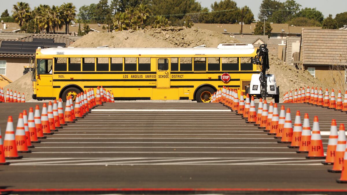 An LAUSD school bus with a bunch of traffic cones in front of it in a parking lot