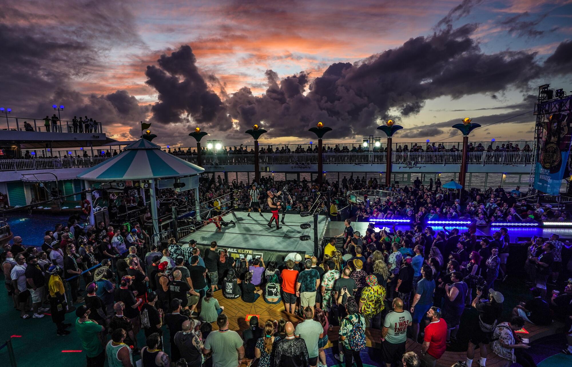 People watch a wrestling match on a cruise ship, with a sunset in the background