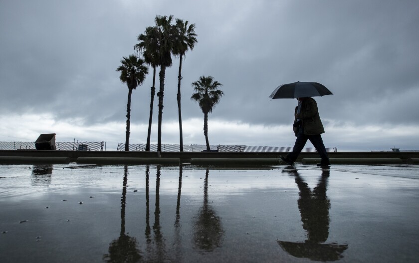 A pedestrian with an umbrella walks along the beach path in Santa Monica 