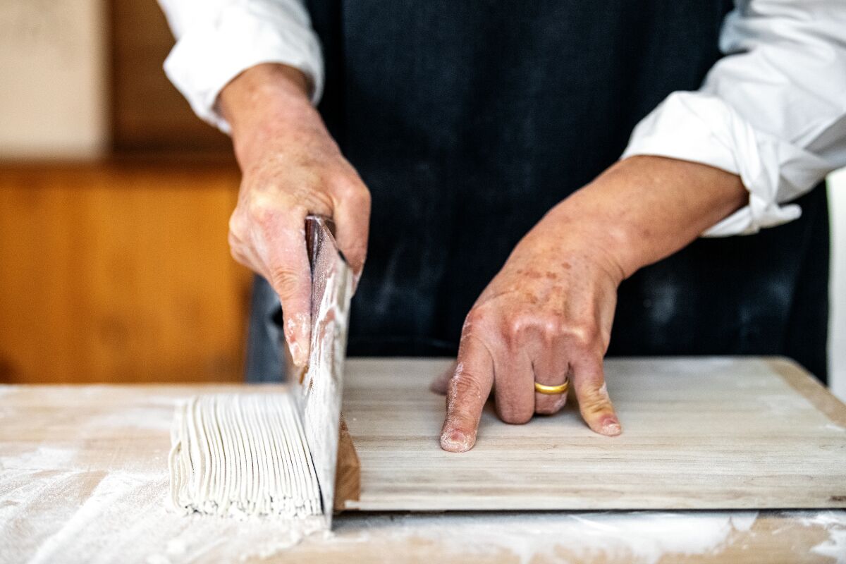 A close-up of Sakai's hands cutting fresh soba noodles.