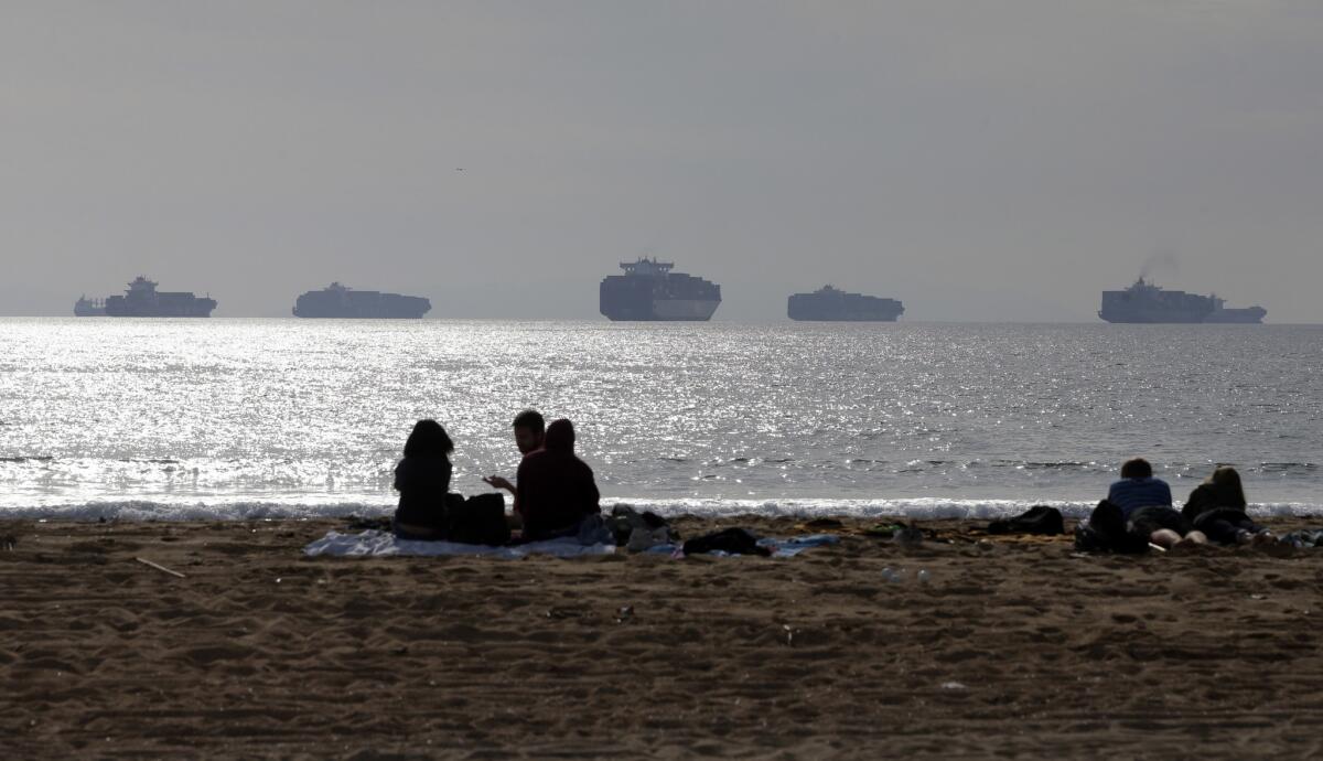 People sit on the sand in Sunset Beach near the ports of Long Beach and Los Angeles during the West Coast ports dispute in February. The ports slowdown was a key factor in the U.S. first quarter economic contraction, which has pulled down the International Monetary Fund's forecast for global growth forecast this year.