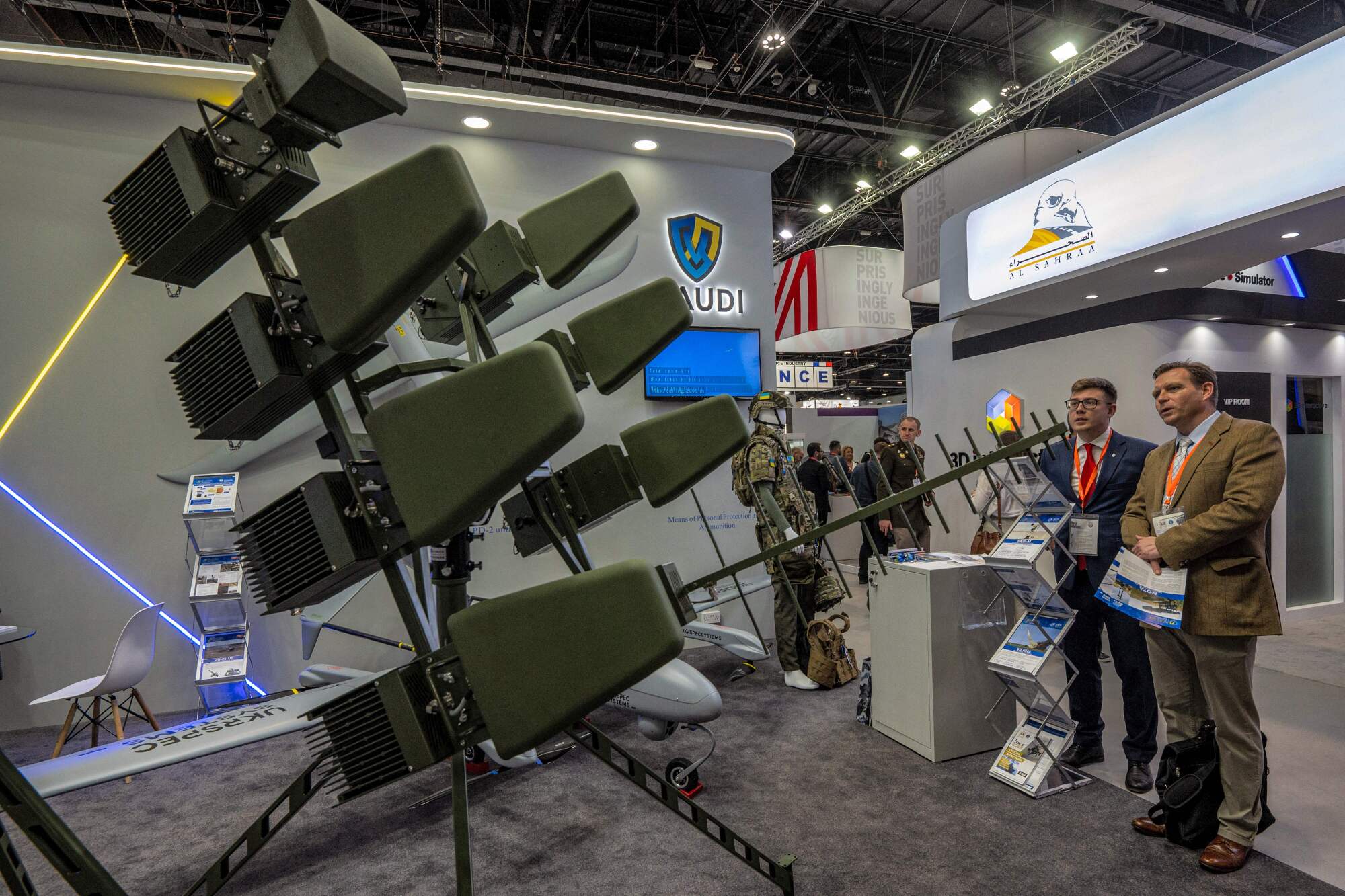 Two men in suits, standing to the right, view a device on a stand with an antenna 