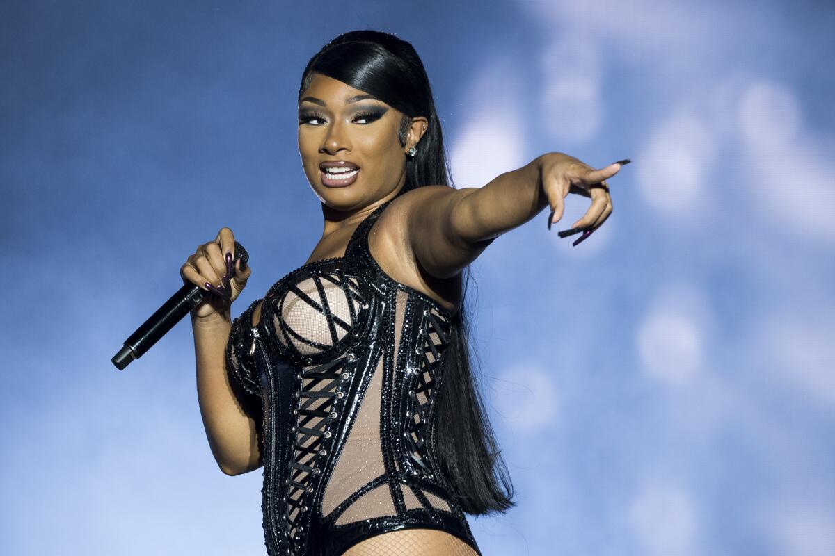 Megan Thee Stallion points to the crowd while holding a mic in the other hand and wearing a black corset leotard. 