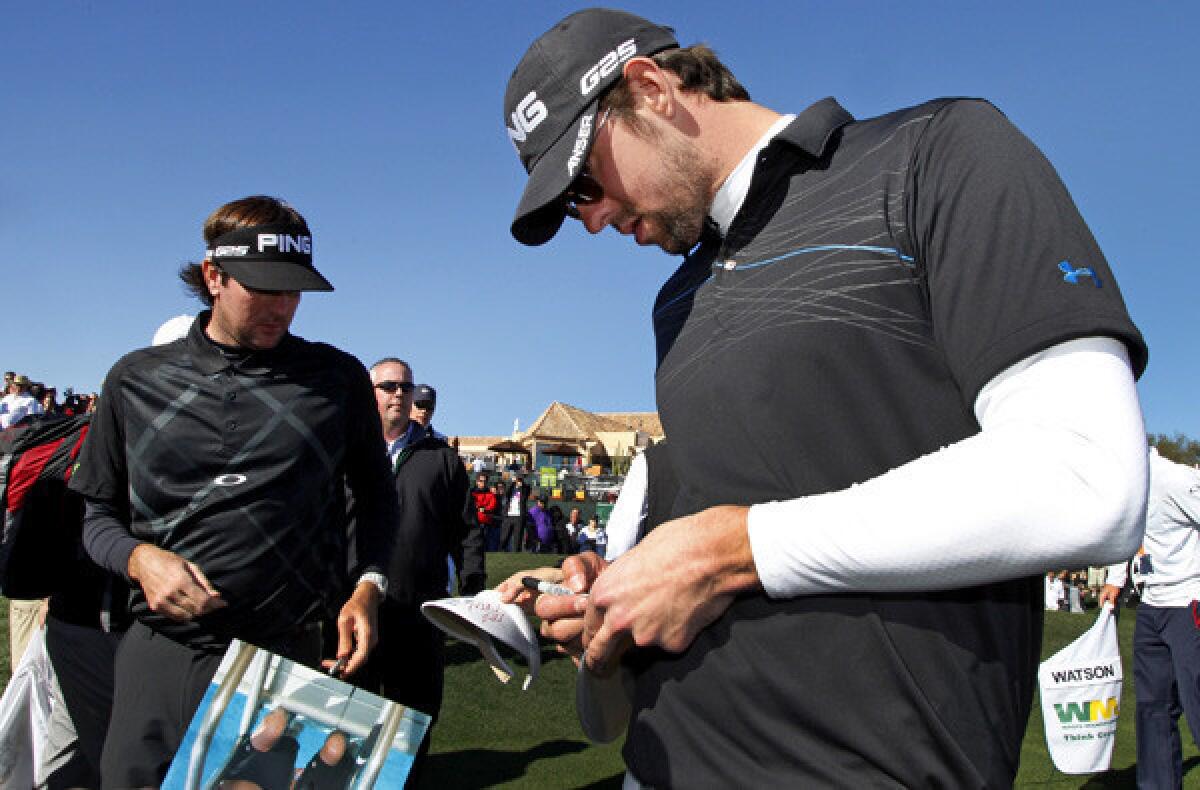 Michael Phelps signs an autograph as he and playing partner Bubba Watson leave the 18th green in Scottsdale, Ariz.