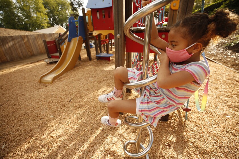 A kindergartener wears a face mask while on playground equipment