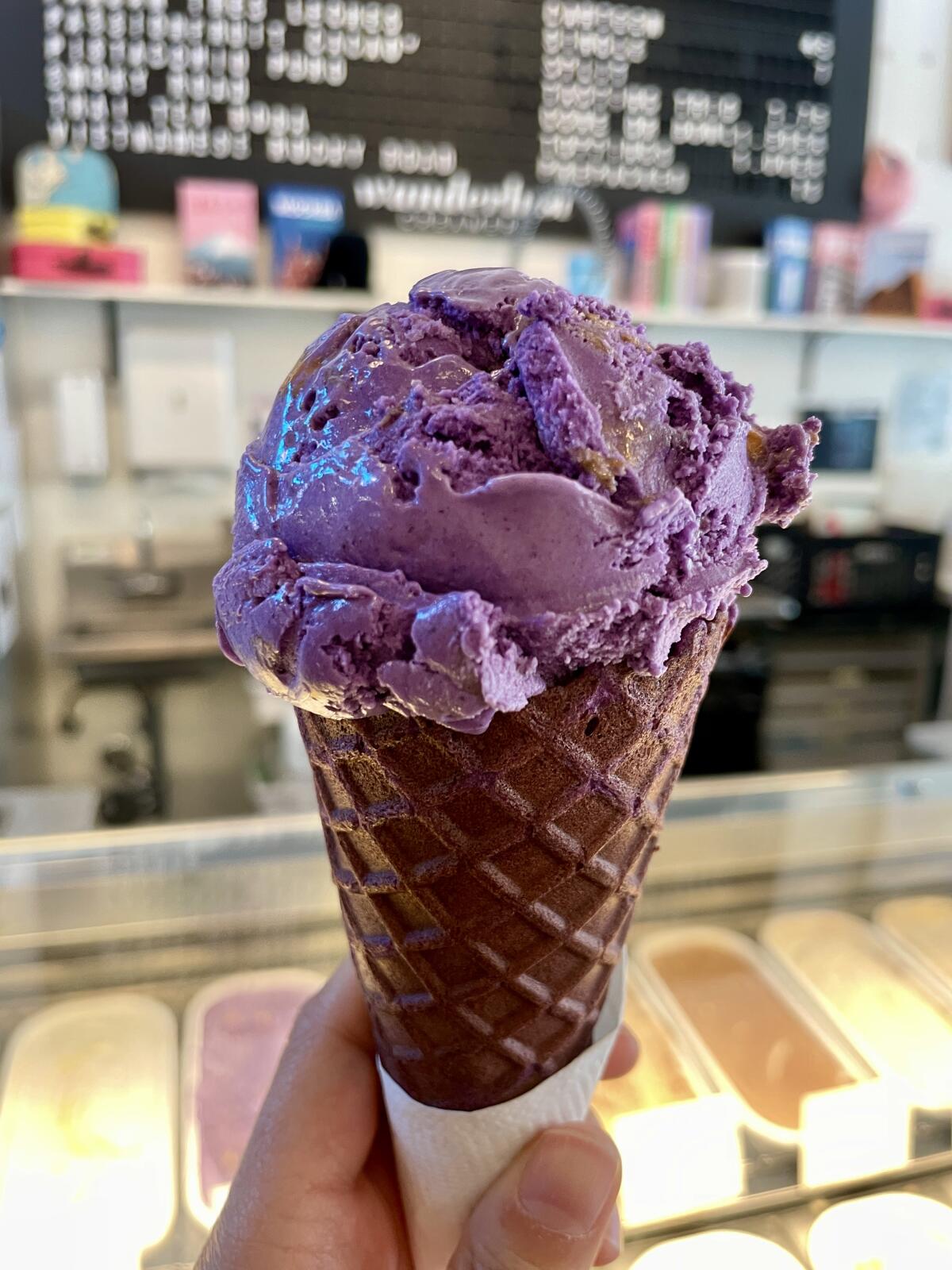 A hand holds up a scoop of purple ice cream in a purple-tinged cone
