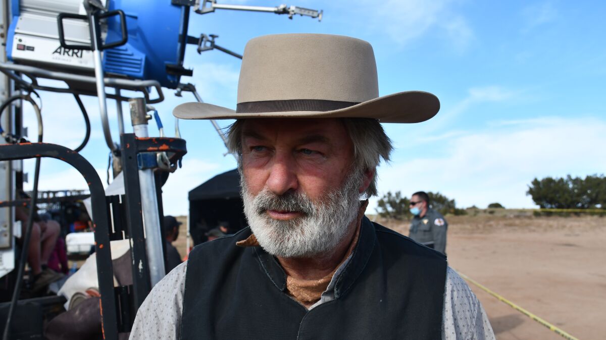A photo shows bearded Alec Baldwin in a western hat standing beside filming equipment.