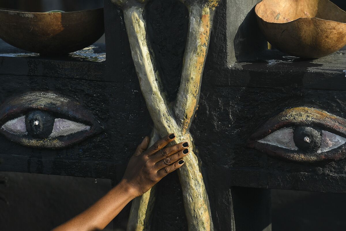 A person touches a monument to Baron Samedi and Gede during a ceremony honoring the Haitian Vodou spirit at the National Cemetery in Port-au-Prince, Haiti, Monday, Nov. 1 2021. Followers of Vodou are marking the Fete Gede celebration of the spirits, equivalent to the Roman Catholic festivity of the Day of the Dead and All Saints Day. (AP Photo/Matias Delacroix)