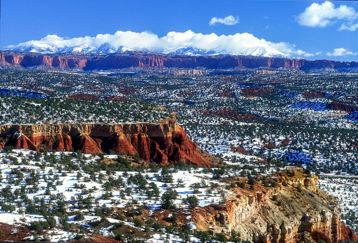 Red rock cliffs in snow-covered landscape with distant mountains. 