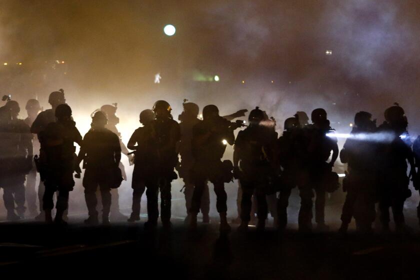 Police walk through a cloud of smoke Aug. 13 as they clash with protesters in Ferguson, Mo.