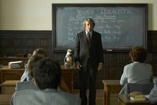 A teacher instructs a class of boys with the aid of a penguin standing on his desk.