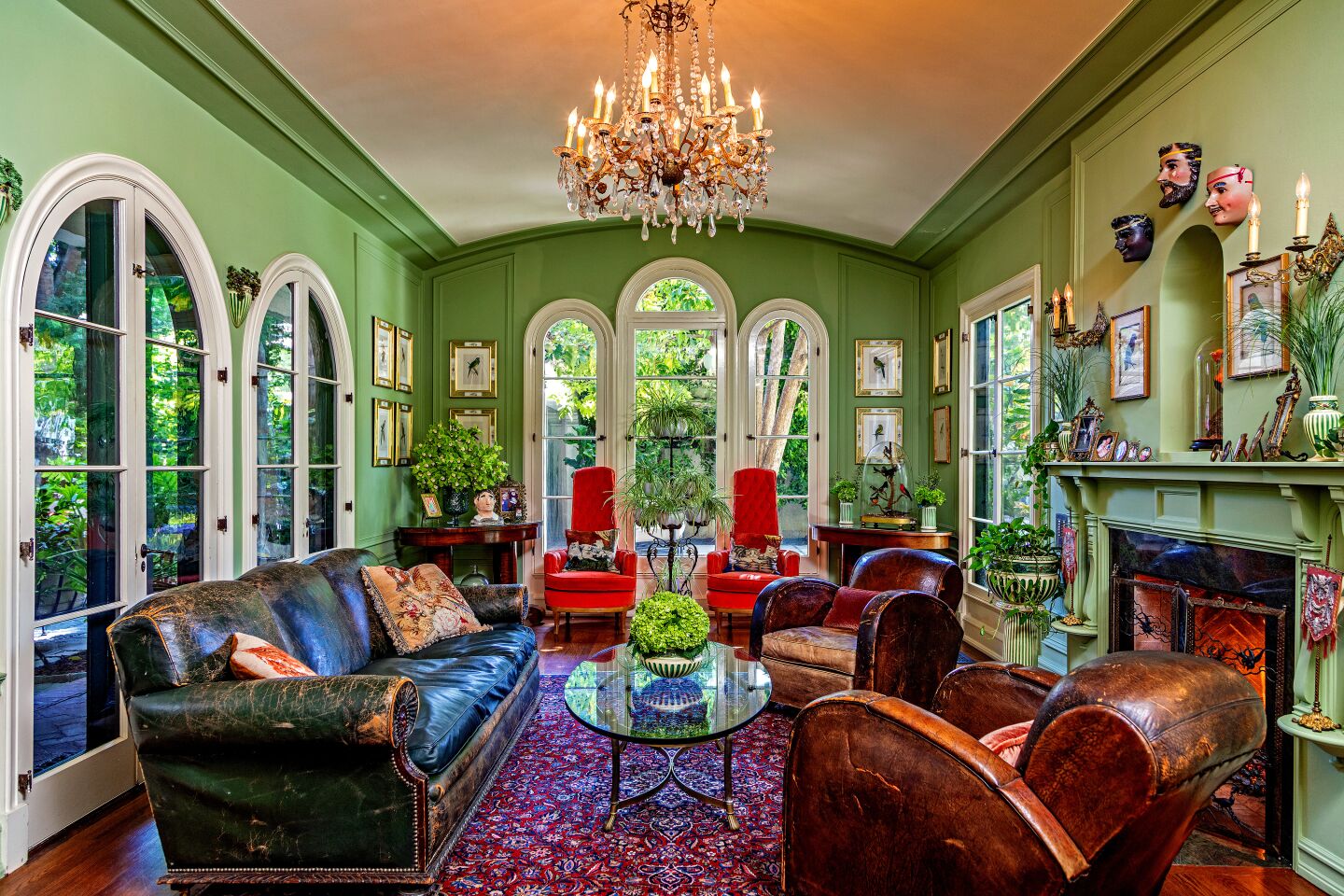 The family room with light green walls, windows overlooking greenery, living room furniture, chandelier and a fireplace.