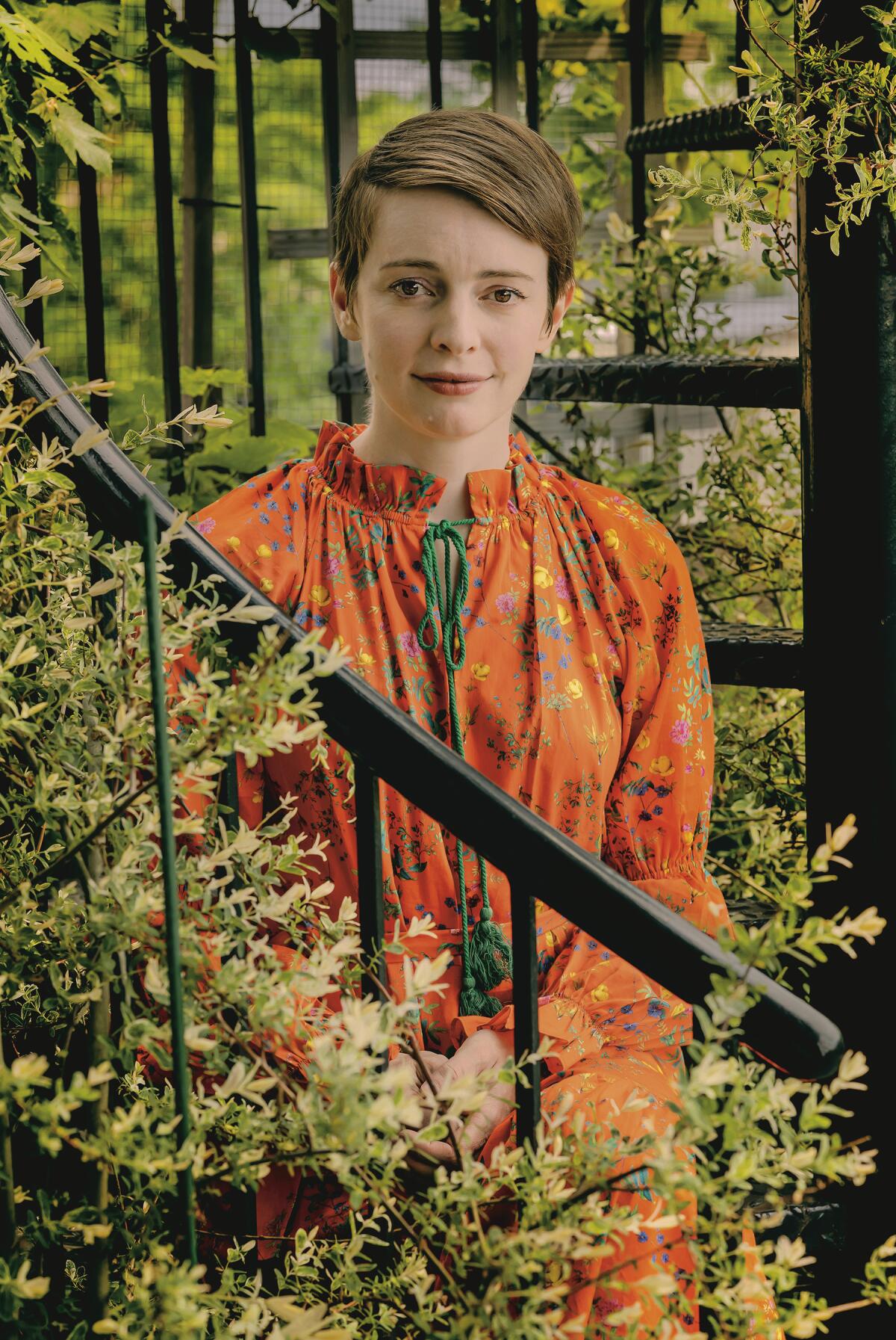 A woman in an orange dress sits on an outdoor spiral staircase.