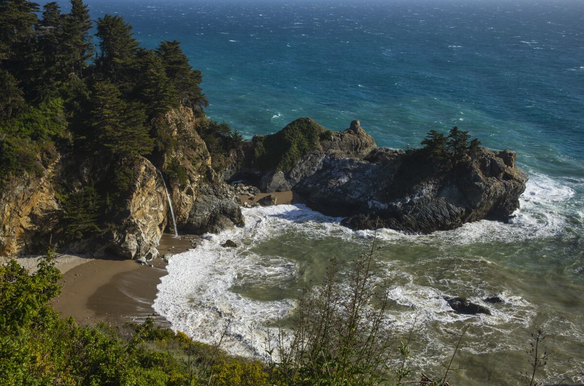 Aerial view of a rocky beach inlet with water flowing from a cliffside.