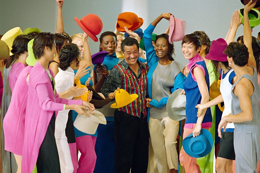 A man in a dark green shirt and bright striped vest is surrounded by women in brightly colored ensembles.