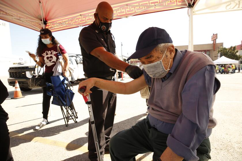 LOS ANGELES, CA - FEBRUARY 24: She Tang Tan, 80, receives the Pfizer COVID-19 vaccine from LA City Fire Captain Paramedic Leon Dunn as the LA City CORE mobile team is staging a vaccination clinic in Chinatown for senior citizens, in an attempt to improve access to the vaccine among vulnerable populations. Chinatown on Wednesday, Feb. 24, 2021 in Los Angeles, CA. (Al Seib / Los Angeles Times).