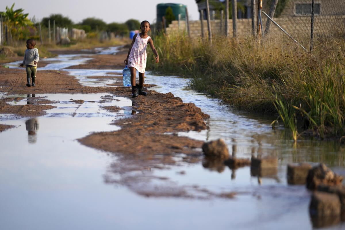 A young girl with a water bottle and her brother walk through a flooded street in Pretoria, South Africa.