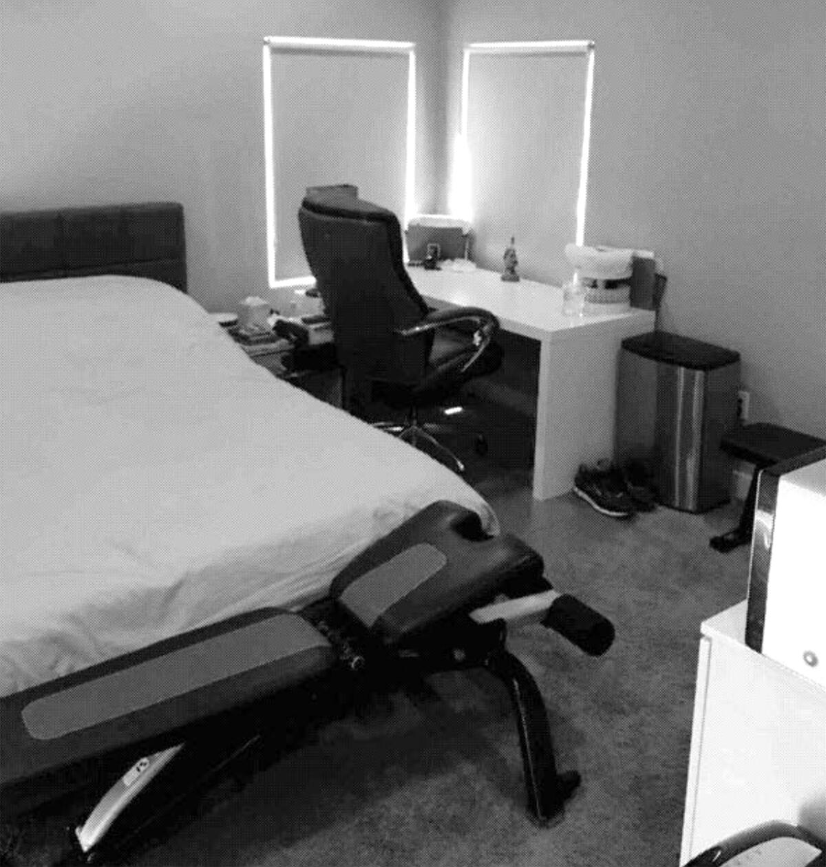 A room with a bed, exercise equipment and a desk with shades pulled down on two windows.