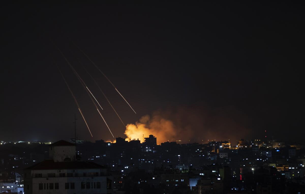An explosion flashes and smoke rises in the distance from a nighttime missile strike.
