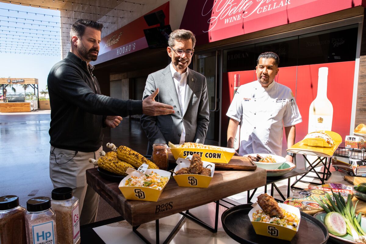Three men talk about a display of food items on a table.