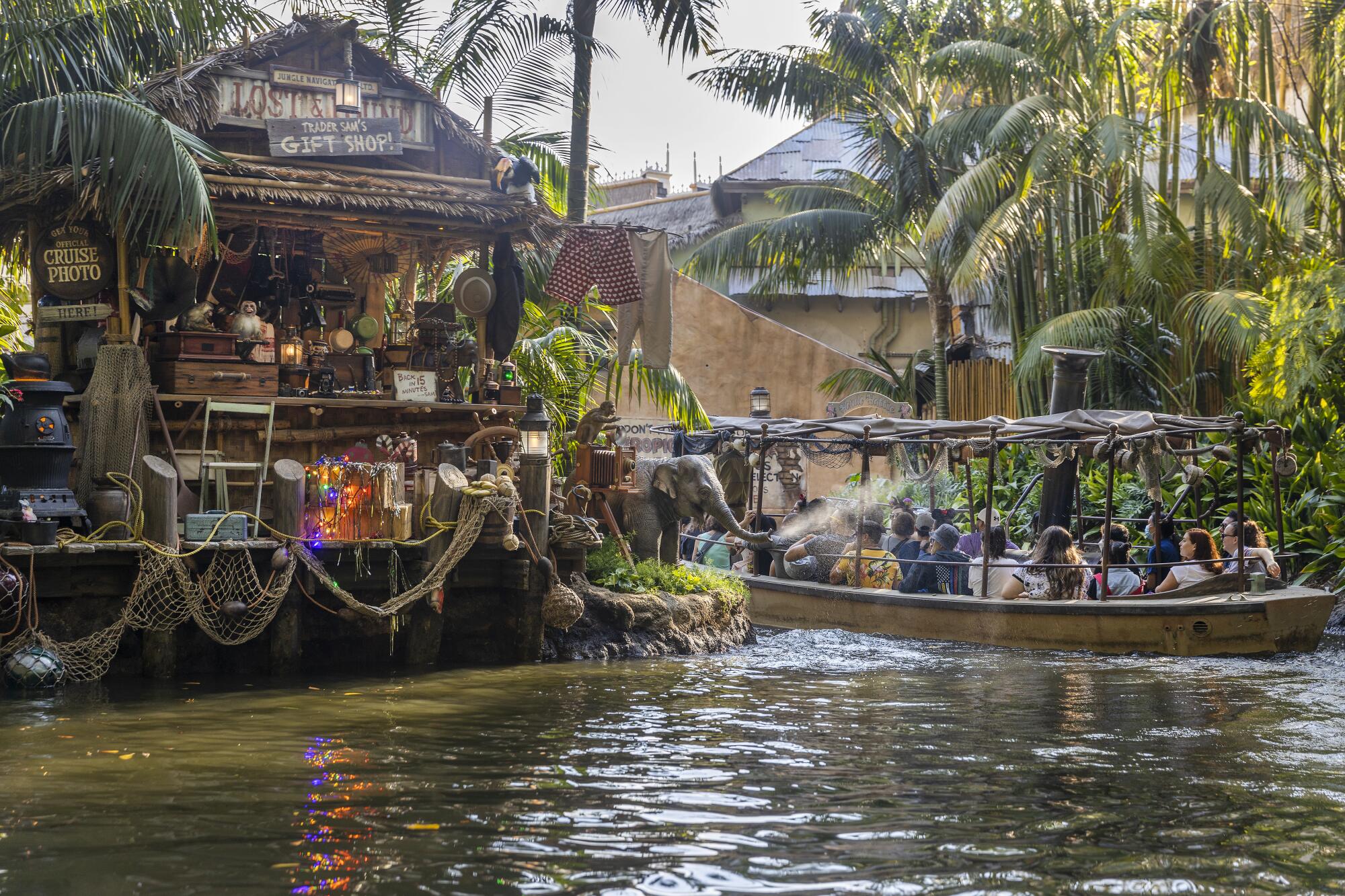 A baby elephant sprays water at a Jungle Cruise boat as they pass by Trader Sam's Gift Shop