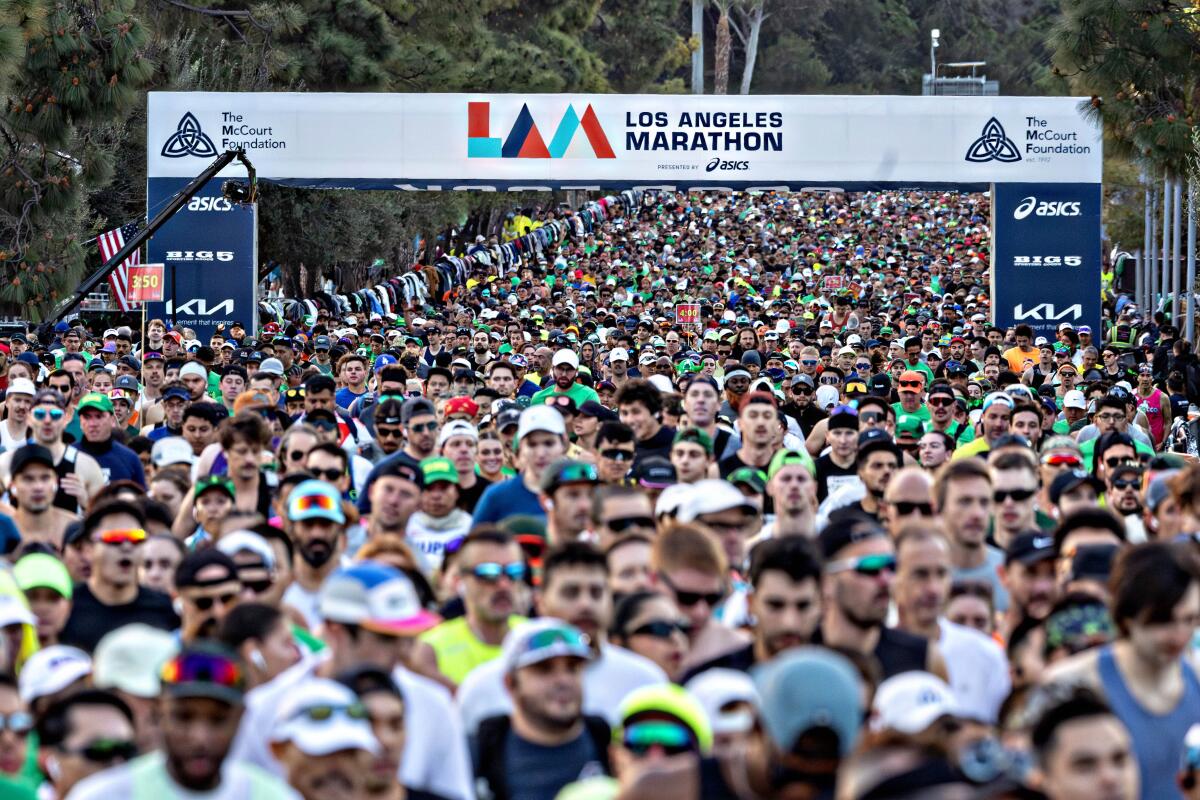 A massive crowd moves beneath a banner that reads "Los Angeles Marathon."