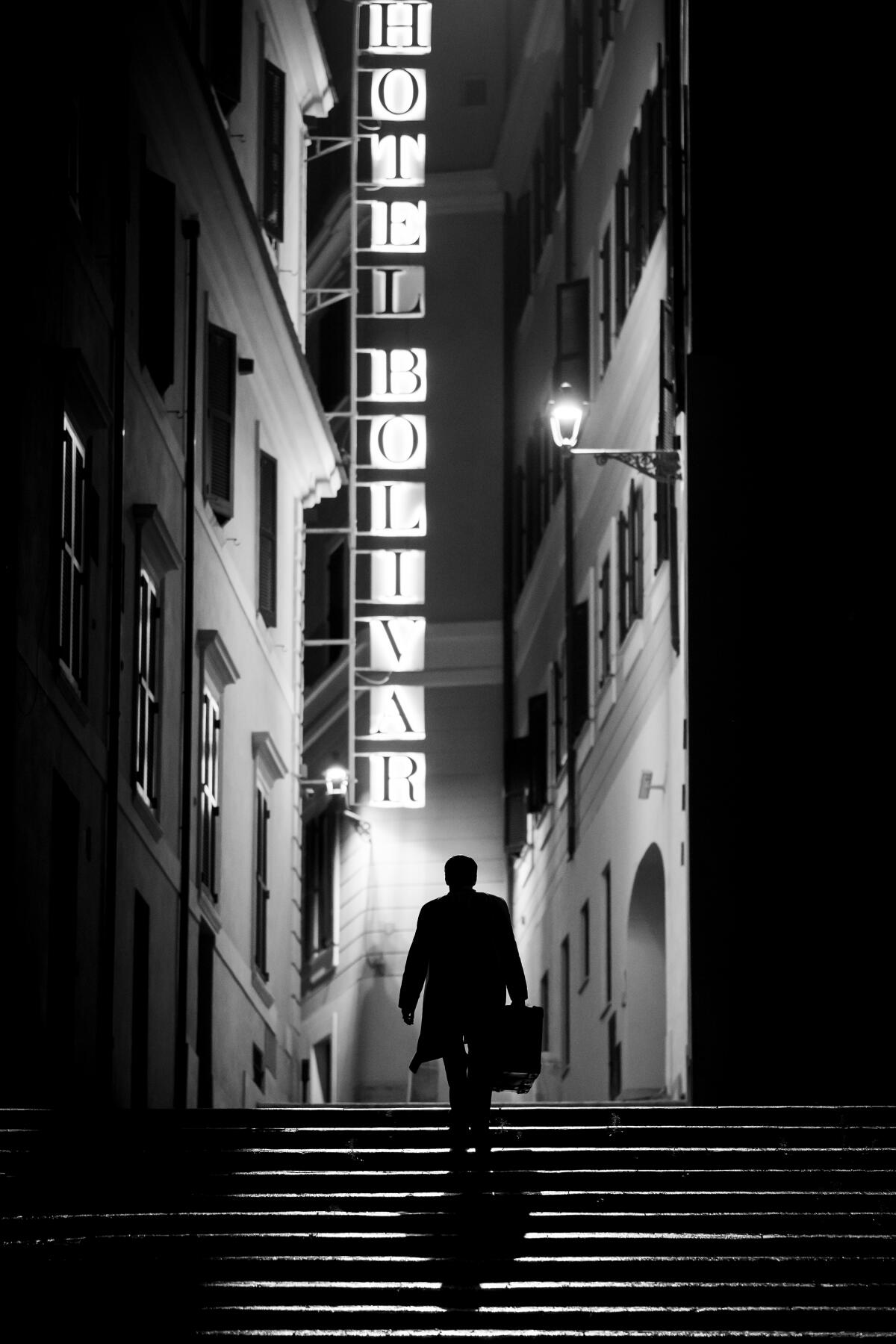  A man walks up a staircase lit by a hotel sign at night in "Ripley."