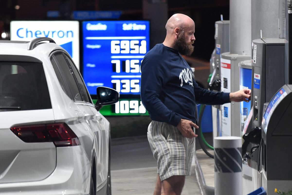 A man pays at the pump with a sign behind him pricing regular gas at $6.95