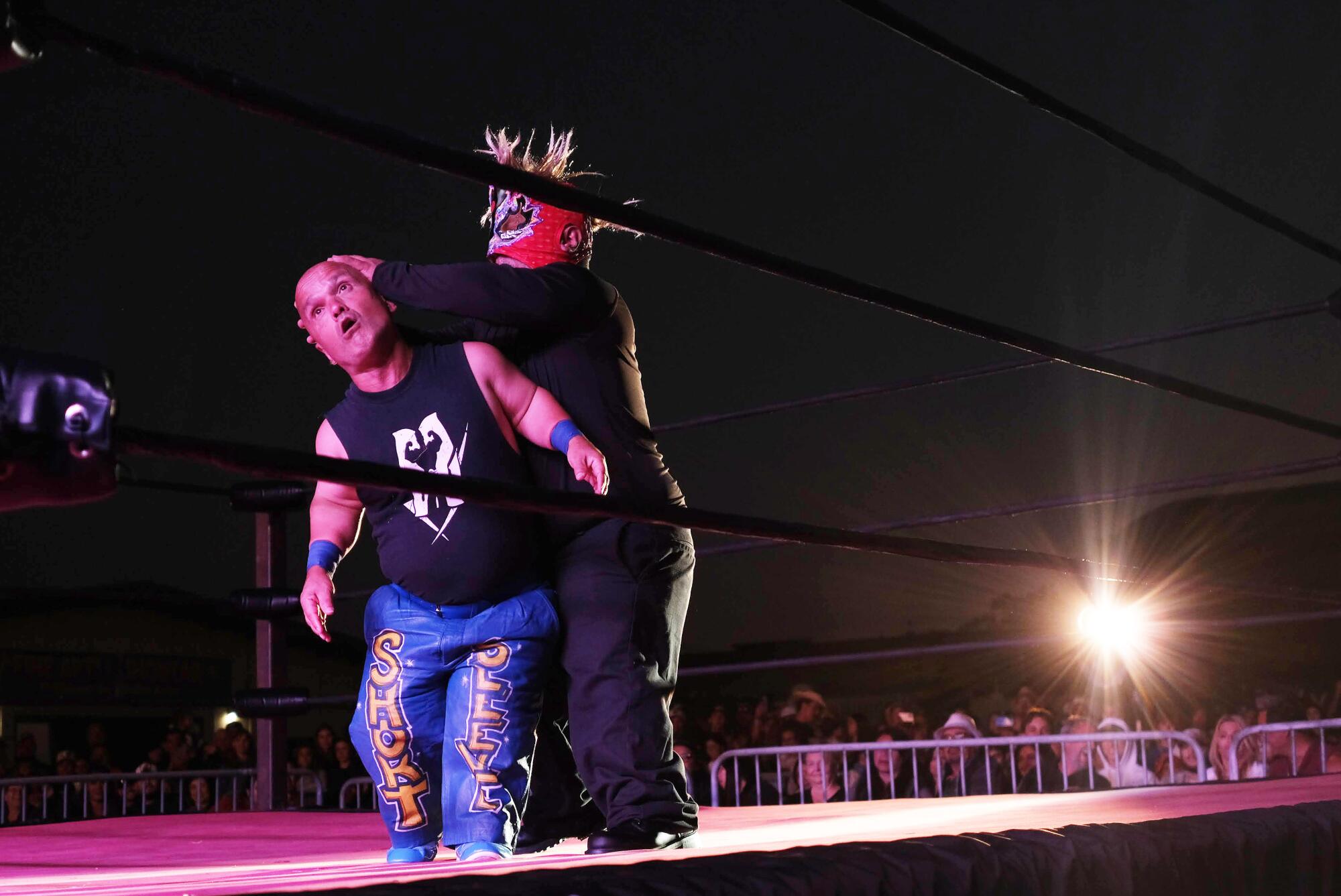 A person grabs the head of another person in a wrestling ring.