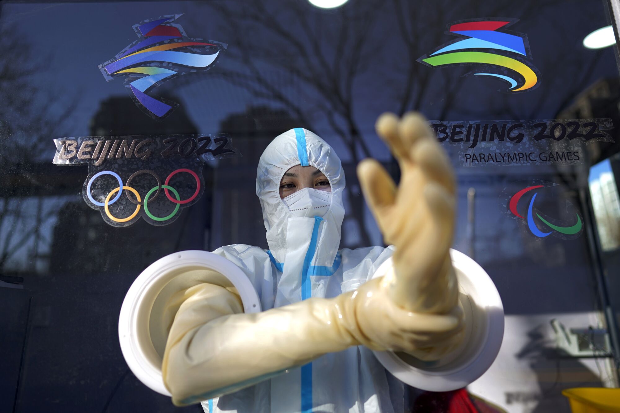 A person in protective suit reaches through two holes in a barrier screen with gloved hands