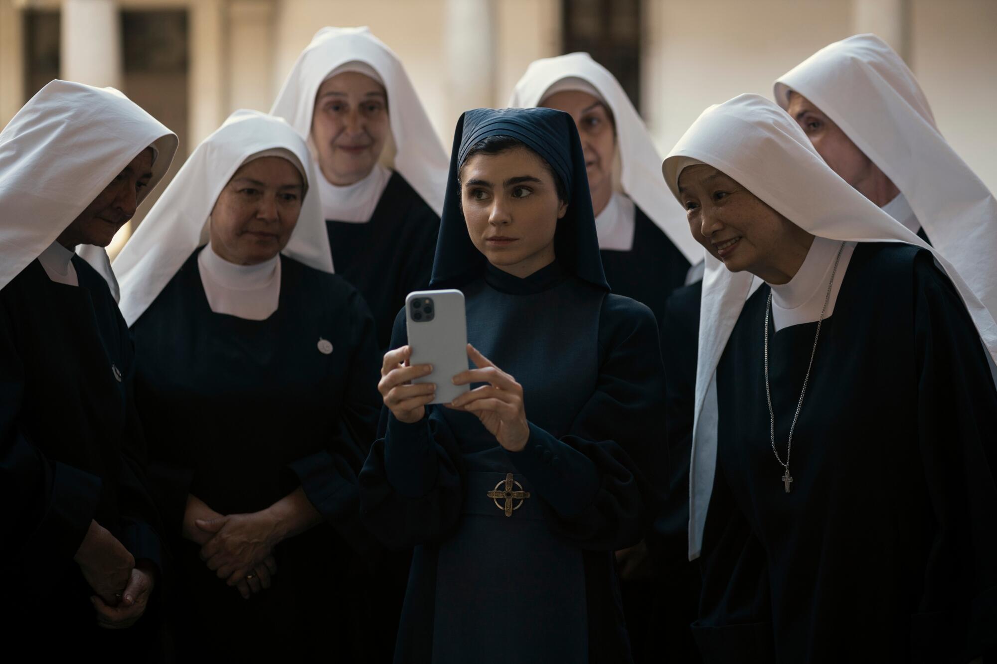 A sister holding a smartphone surrounded by a group of nuns in white habits